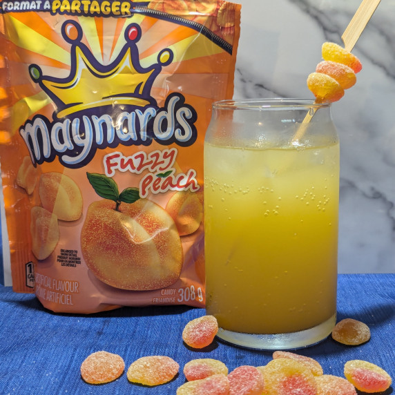 A glass of fuzzy peach cocktail with a bag of fuzzy peach candies.