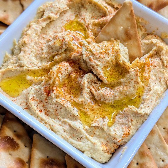 A bowl of smoked hummus with a pita chip dipped in it. 