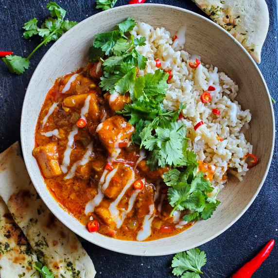 A bowl of bright red paneer tikka, green cilantro, and white rice with a black background