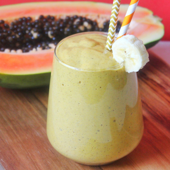 papaya-banana lactation smoothie served in a glass with a straw. Papaya in the background. 