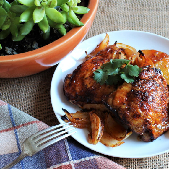 A white plate with paprika chicken, potatoes and sweet onions. 