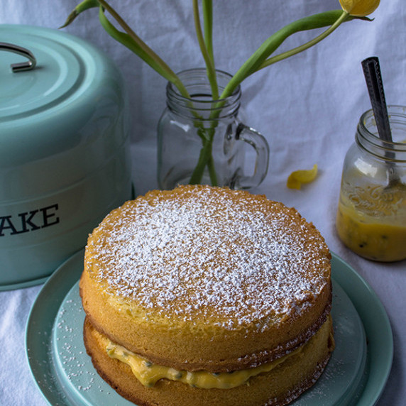 two layer victoria sponge cake with passion fruit filling on a blue plate with flowers in the backgr