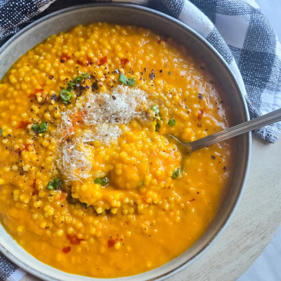 Gorgeously golden soup with pops of red & green against a checkered towel.