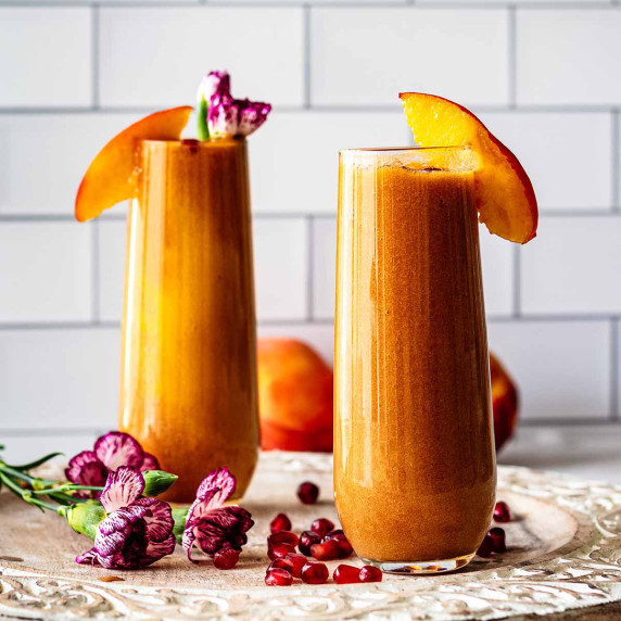 Two tall glasses of peach juice topped with fresh peach slices.