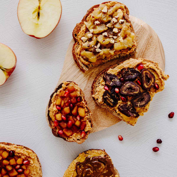 Overhead view of peanut butter toast with various toppings on a light wood cutting board