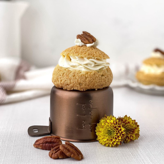pecan pie cream puff on top of an overturned measuring cup with a pecan on top and scattered nearby