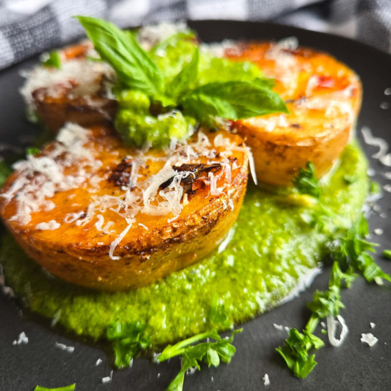 Golden brown potato medallions on a bed of vibrant green pesto with green herbs.