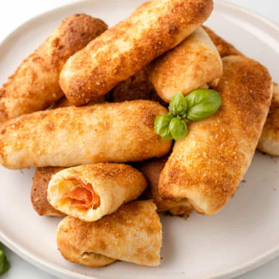 Pepperoni rolls stacked on a plate with one cut in half to see inside.