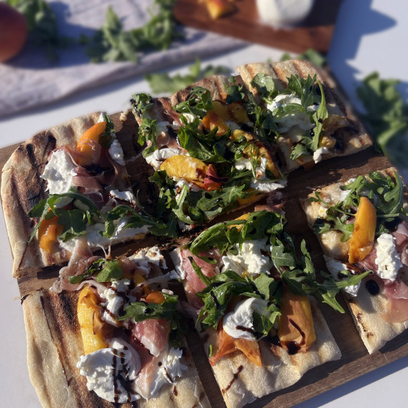 grilled pizza dough topped with burrata, peaches, prosciutto and arugula