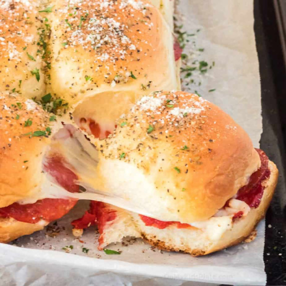 Cheesy pizza slider being pulled apart from the other sandwiches on the pan.