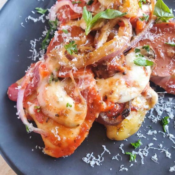 A cheesy pile of pierogies topped with pizza toppings and green herbs on a black plate.