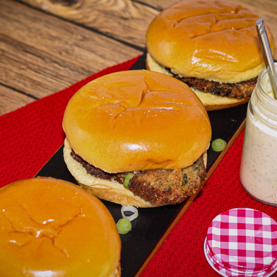 3 Pork Schnitzel Sandwiches with Dill Aioli on a red placemat.