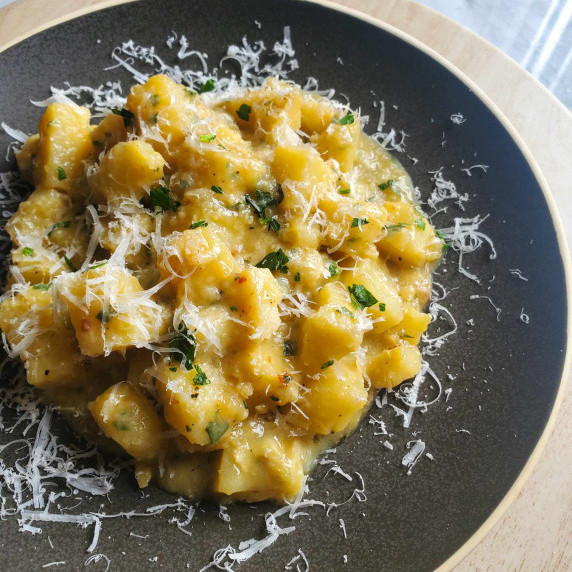 A creamy pile of potatoes with pops of green and white on a matte black plate.