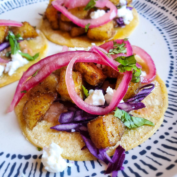 Vibrant pickled onions sit a top crispy potatoes and purple cabbage.