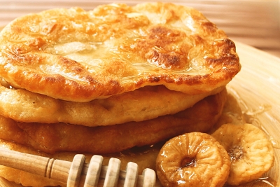 A stack of golden pulled pitas — small, hand‑stretched fried flatbreads — with honey and dried figs.