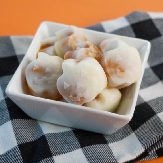 Frozen pumpkin yogurt bites snack close up and shaped like mini pumpkins sit in a small white bowl.