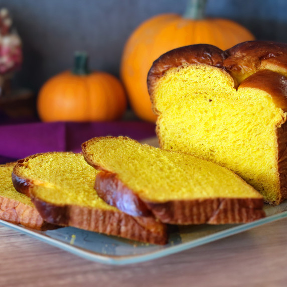 Pumpkin brioche sliced to show interior crumb on a glass serving platter.