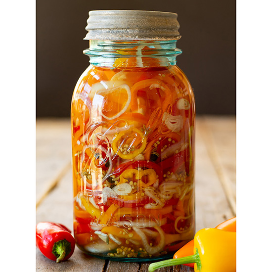 A vintage Ball jar filled with multi-colored mini peppers and shallots.