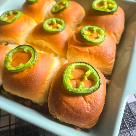 A dish full of golden sliders topped with green jalapeno rings.