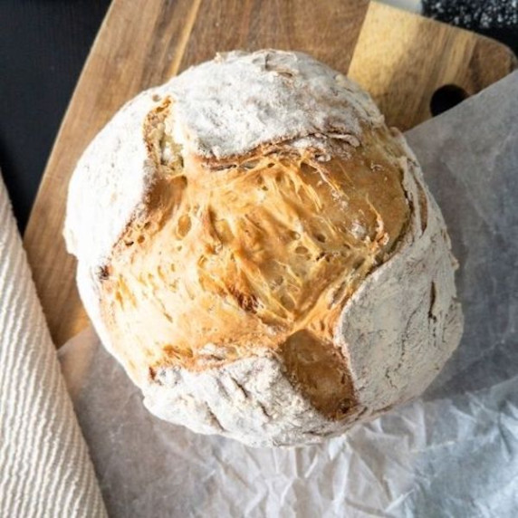 Irish soda bread on a wooden cutting board with a beige towel in the background.