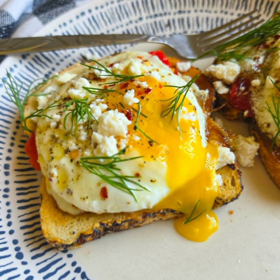 A perfectly fried egg with golden yolk cascading down onto a white plate.