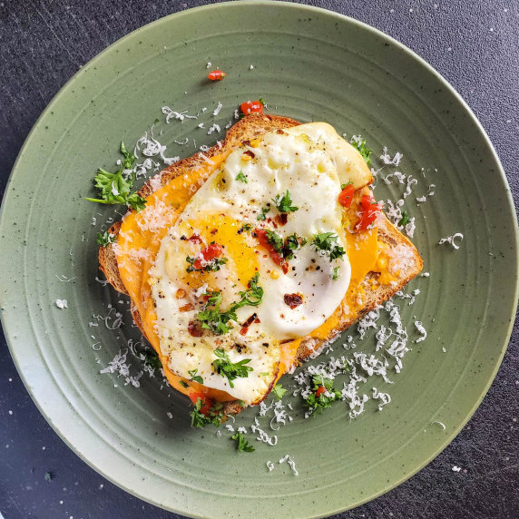 A piece of toast topped with a fried egg on a green plate against a black background.
