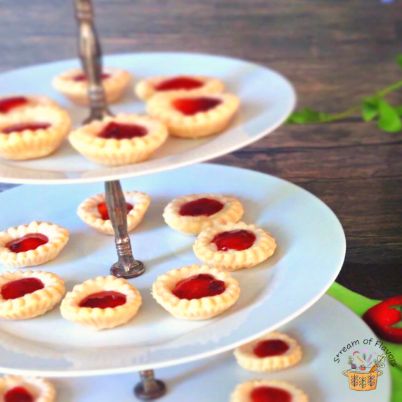 Raspberry jam tarts on a white dessert stand on a wooden background with a napkin and fresh berries