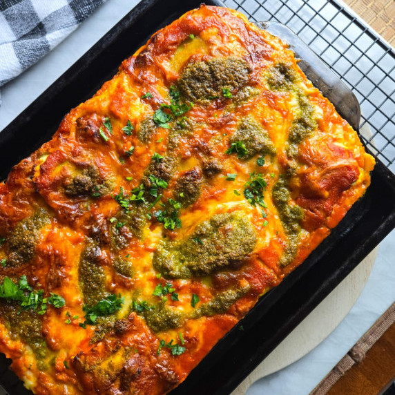 A baking dish full of gorgeously golden ravioli lasagna with pops of green parsley.