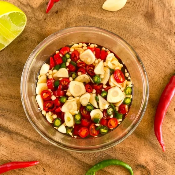 Overhead shot of prik nam pla in a glass cup with a red chili, lime, and garlic on the sides.