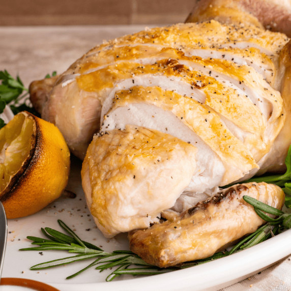 A roast chicken on a white platter, with the breast sliced.