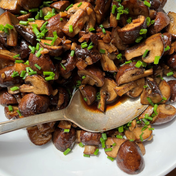 Roasted mushrooms in a wine sauce garnished with fresh chives in a white bowl.