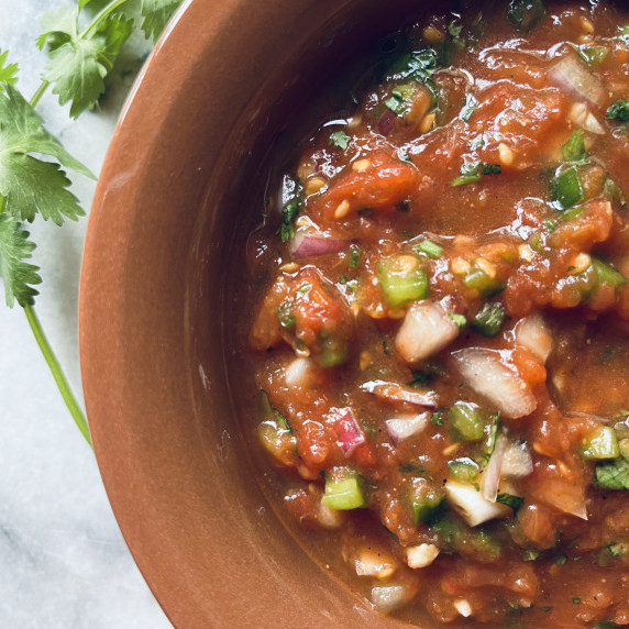 Roasted tomato salsa garnished with cilantro served in a terra cotta salsa bowl.