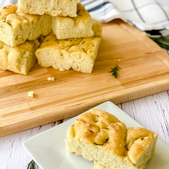 Focaccia on bread with wooden tray in the background holding more focaccia.