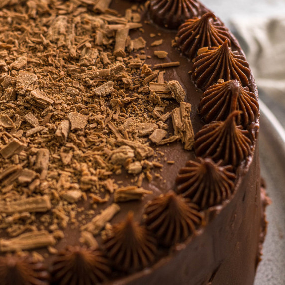 Chocolate cake with cream cheese frosting topped with flaked chocolate pieces.