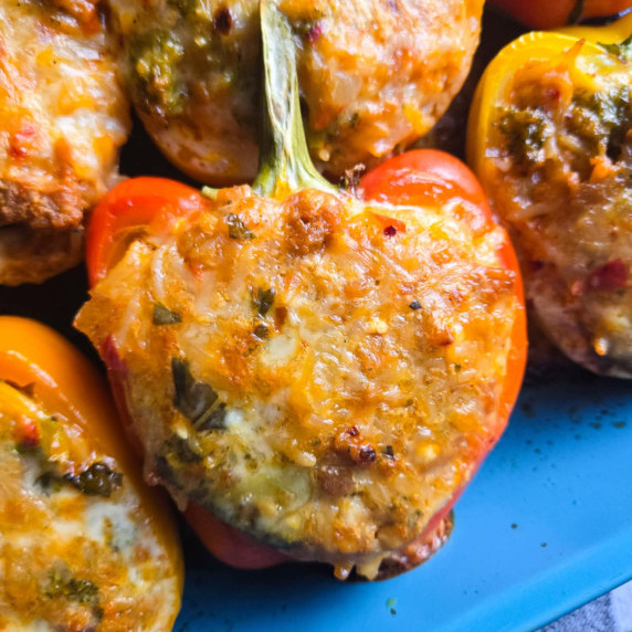 An assortment of colourful peppers in a blue dish with golden, melty cheese.