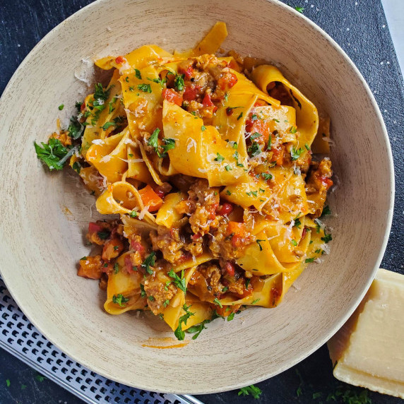 A wooden bowl filled with pasta against a black background.