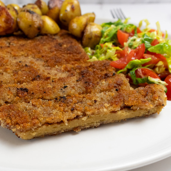 Vegan seitan schnitzel shot from the side with some potatoes and salad on the plate