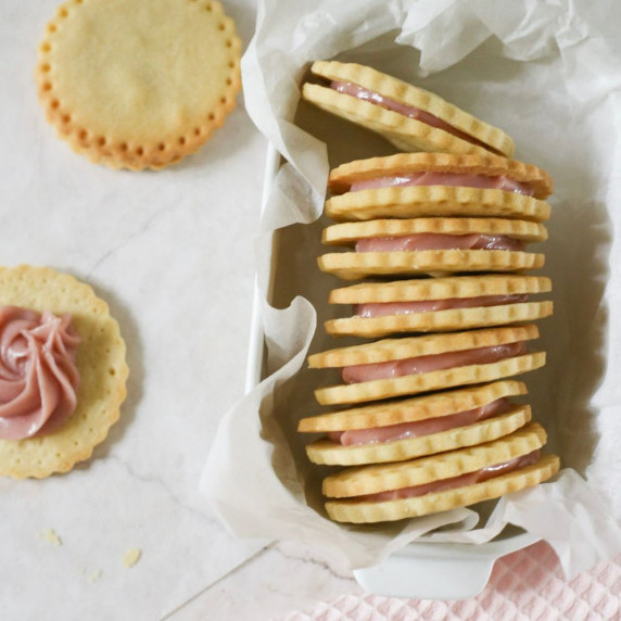 A top down view of some raspberry sandwich cookies in a small baking tin