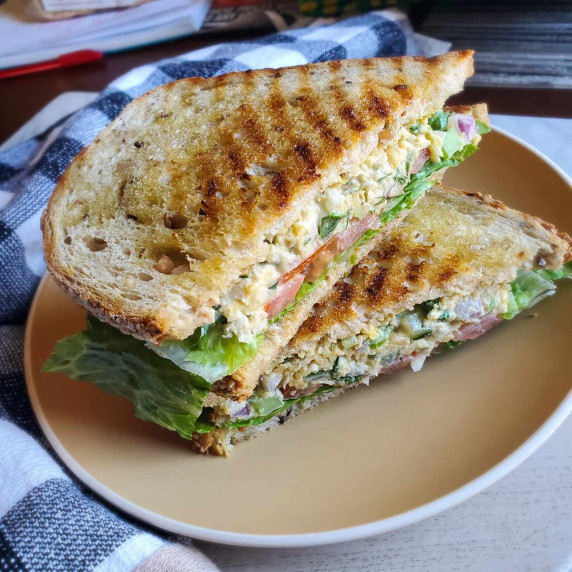Golden, toasted sourdough stuffed with salad on a beige plate.