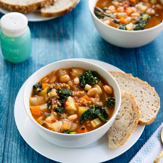Two bowls of soup with a side of sliced bread on a blue wooden table.