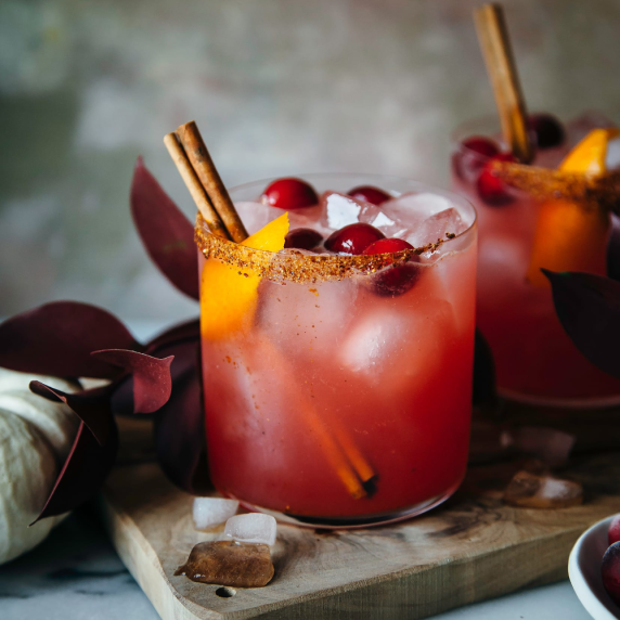 2 glasses of spiced cranberry margarita with a sinnamon sugar rim garnished with orange and cinnamon