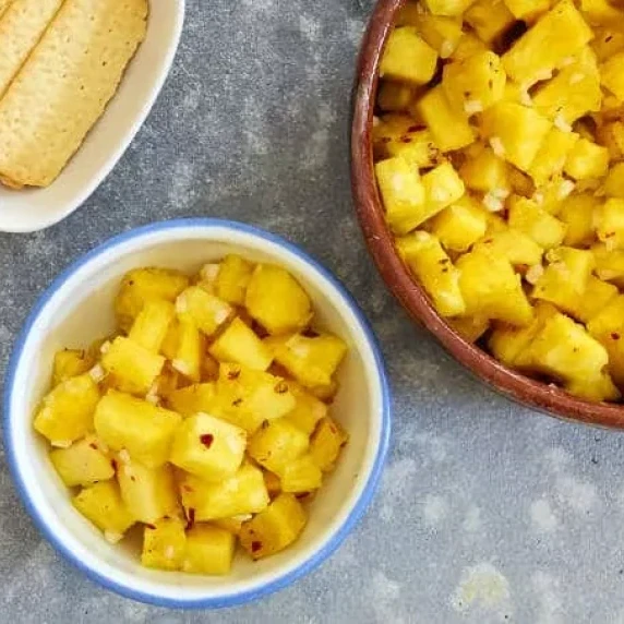 spicy pineapple salad in white bowl with crackers on the side