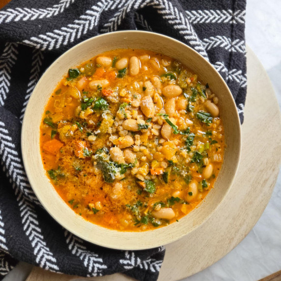 A wooden bowl full of bean and barley soup against a black patterned towel.