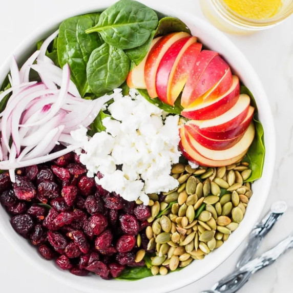 Spinach salad topped with apples and cranberries.