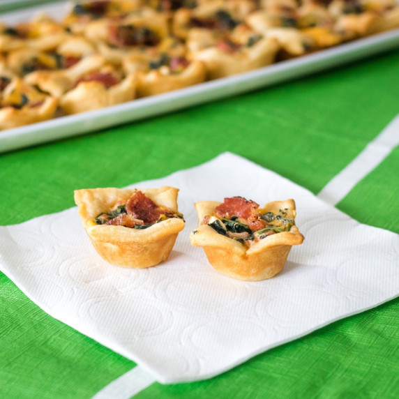 Two spinach dip bites on white napkin. Tray of spinach dip bites in the background.
