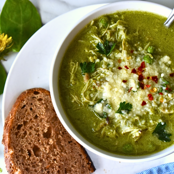 A bowl of spring greens chicken soup, garnished with parmesan and red pepper flakes