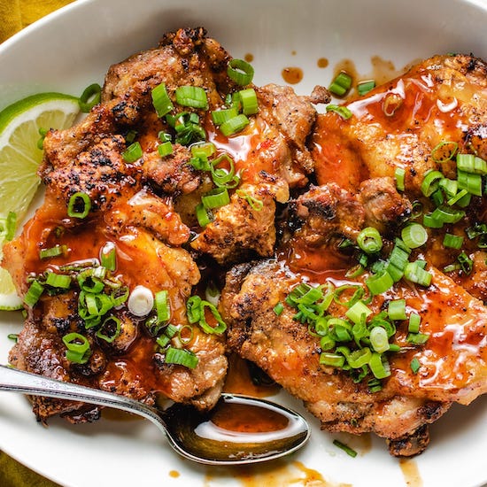 Chicken with honey sriracha sauce, green onions and lime wedges on a white plate with a spoon