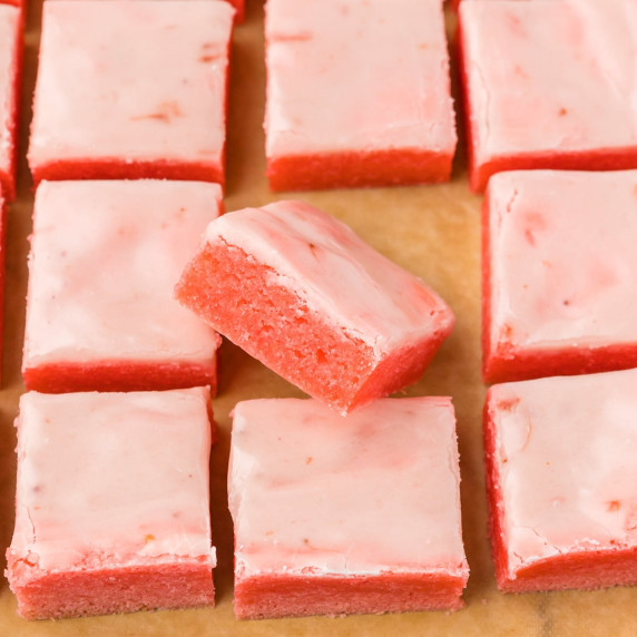 Nine sliced strawberry brownies on parchment paper with one brownie turned to see the chewy edge.