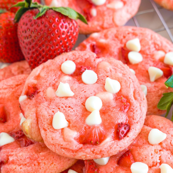 Pink strawberry cookies with white chocolate chips piled together but close up on the top cookie. 