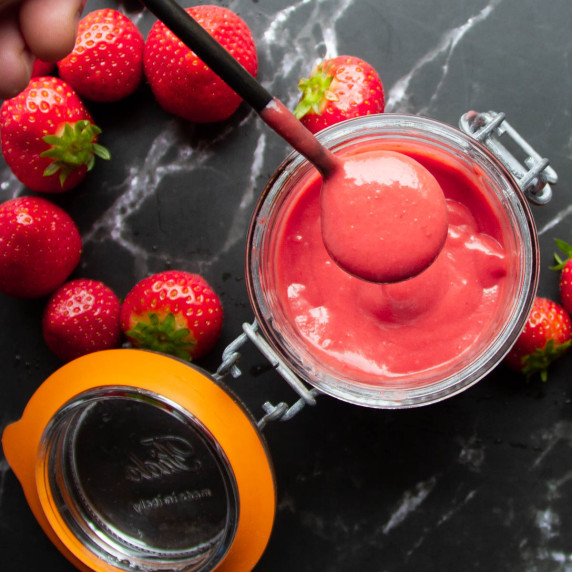 strawberry puree on a spoon over a mason jar with strawberries around.